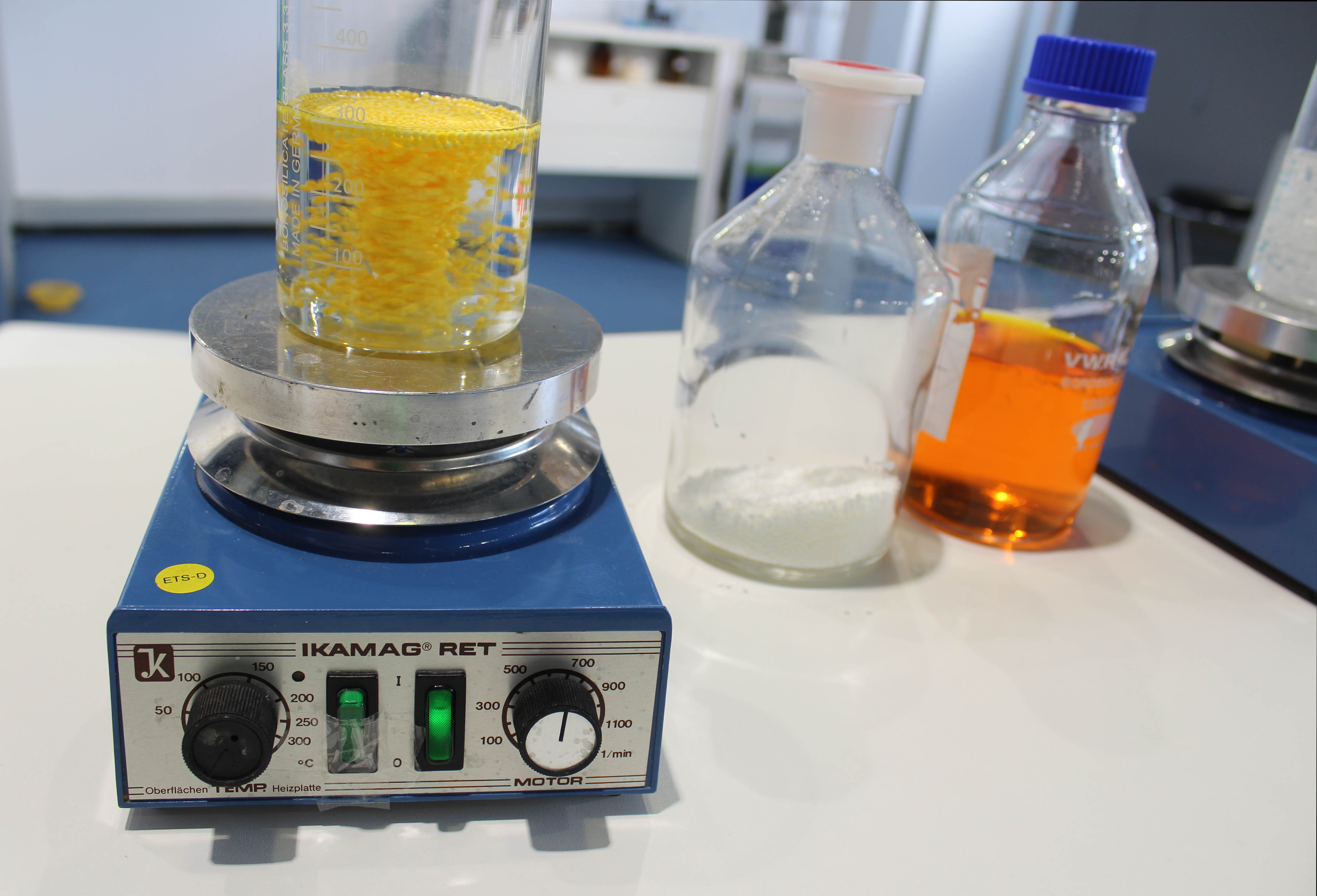 Zu sehen ist eine Reihe von drei Bildern, auf denen in einem Becherglas im Labor die Anlagerung von Stoffen an Plastik demonstriert werden soll.