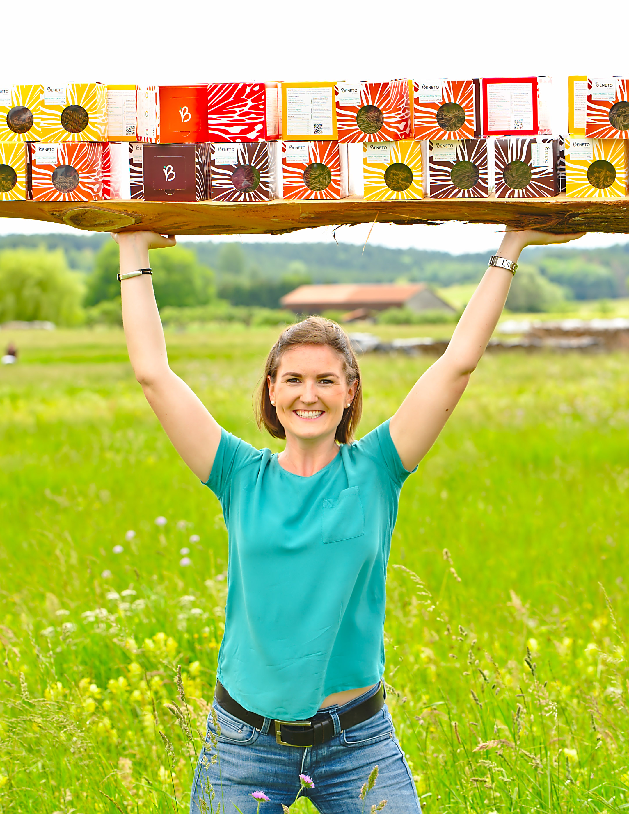 The head of the company in a flowering meadow, lifting a board with many colourful noodle packages.