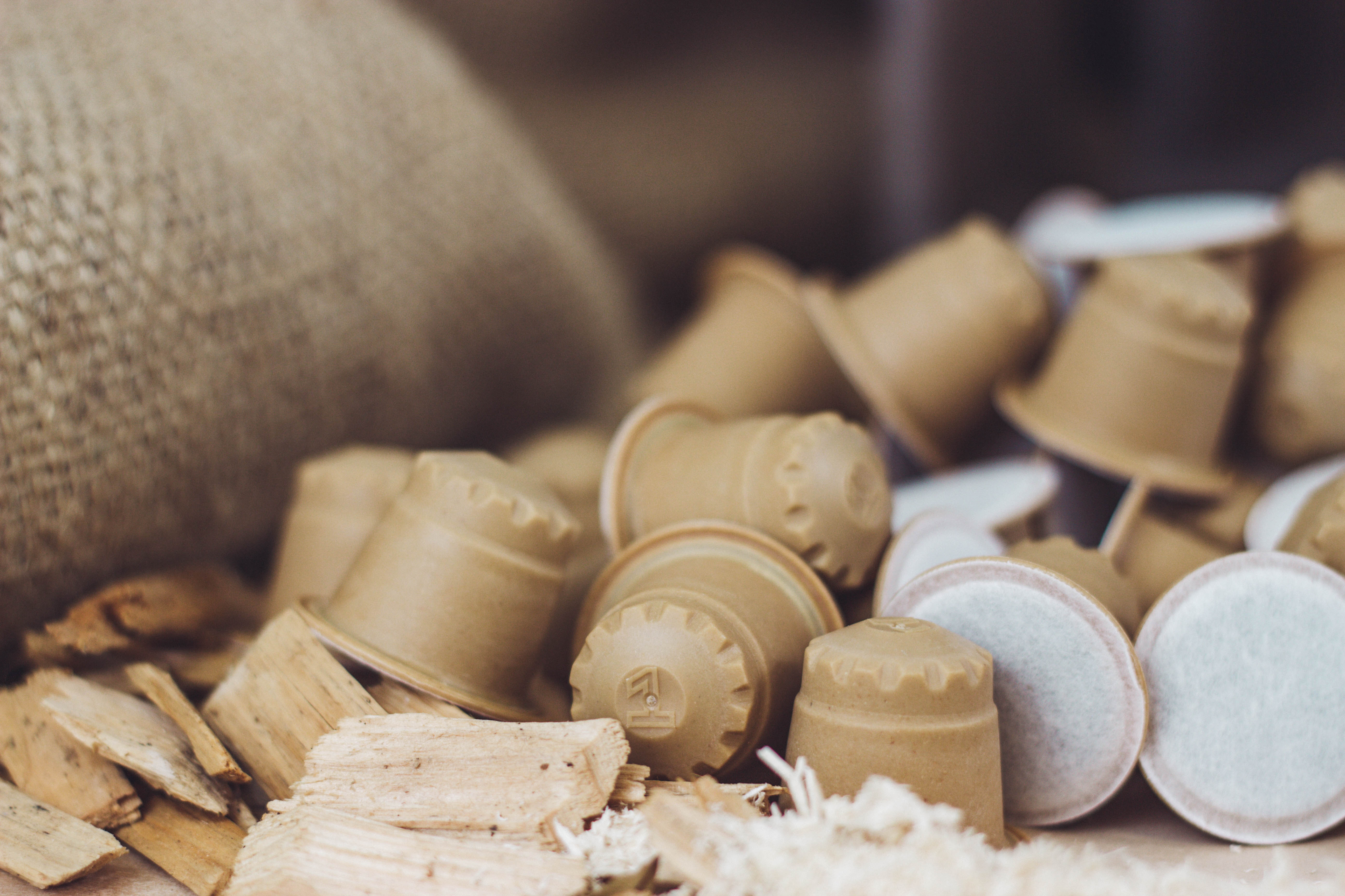 Coffee capsules in front of a jute sack, wood shavings in the foreground.