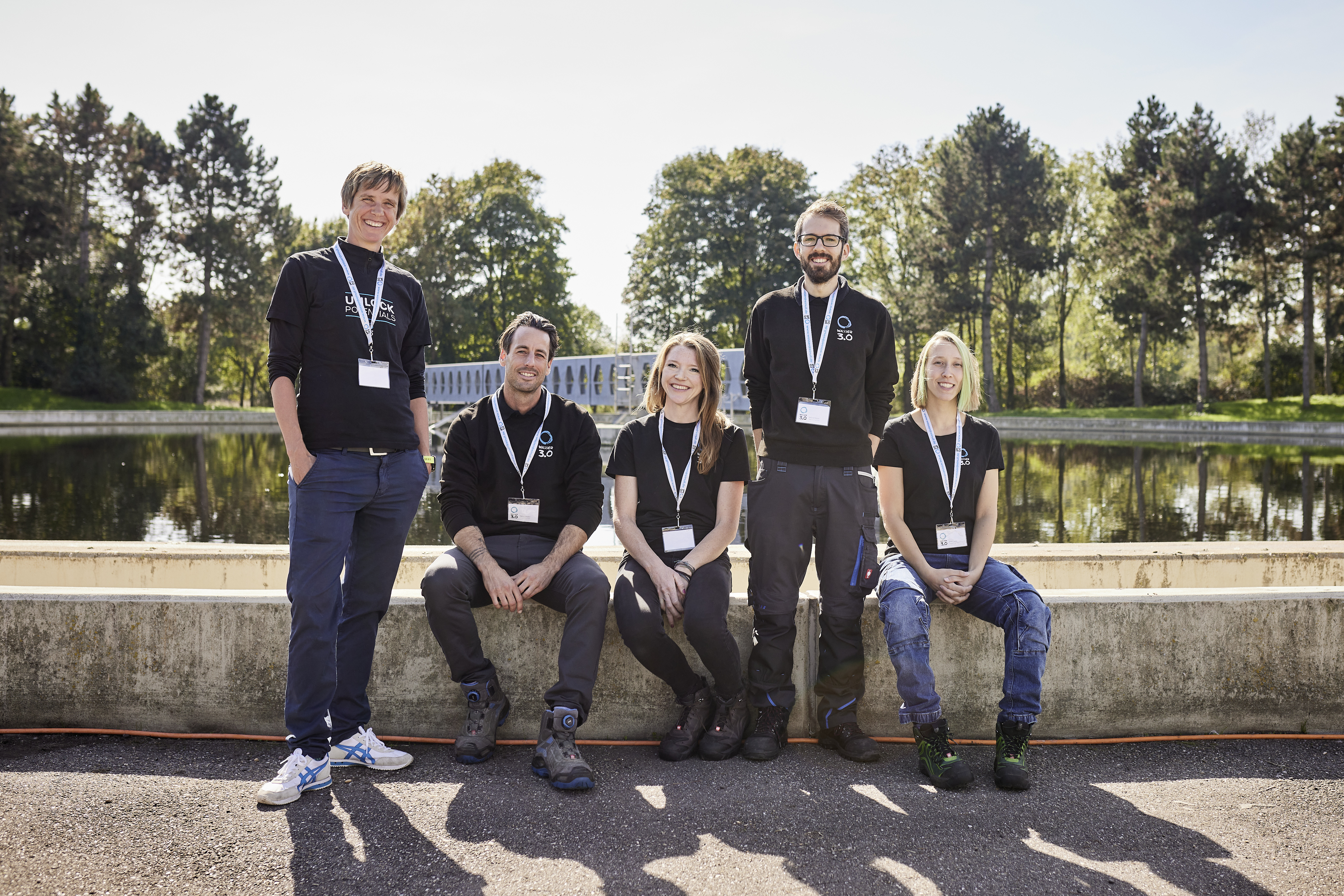Die fünf Abwasserexpertinnen und -experten in schwarzen Sweatshirts vor der Abwasseranlage.