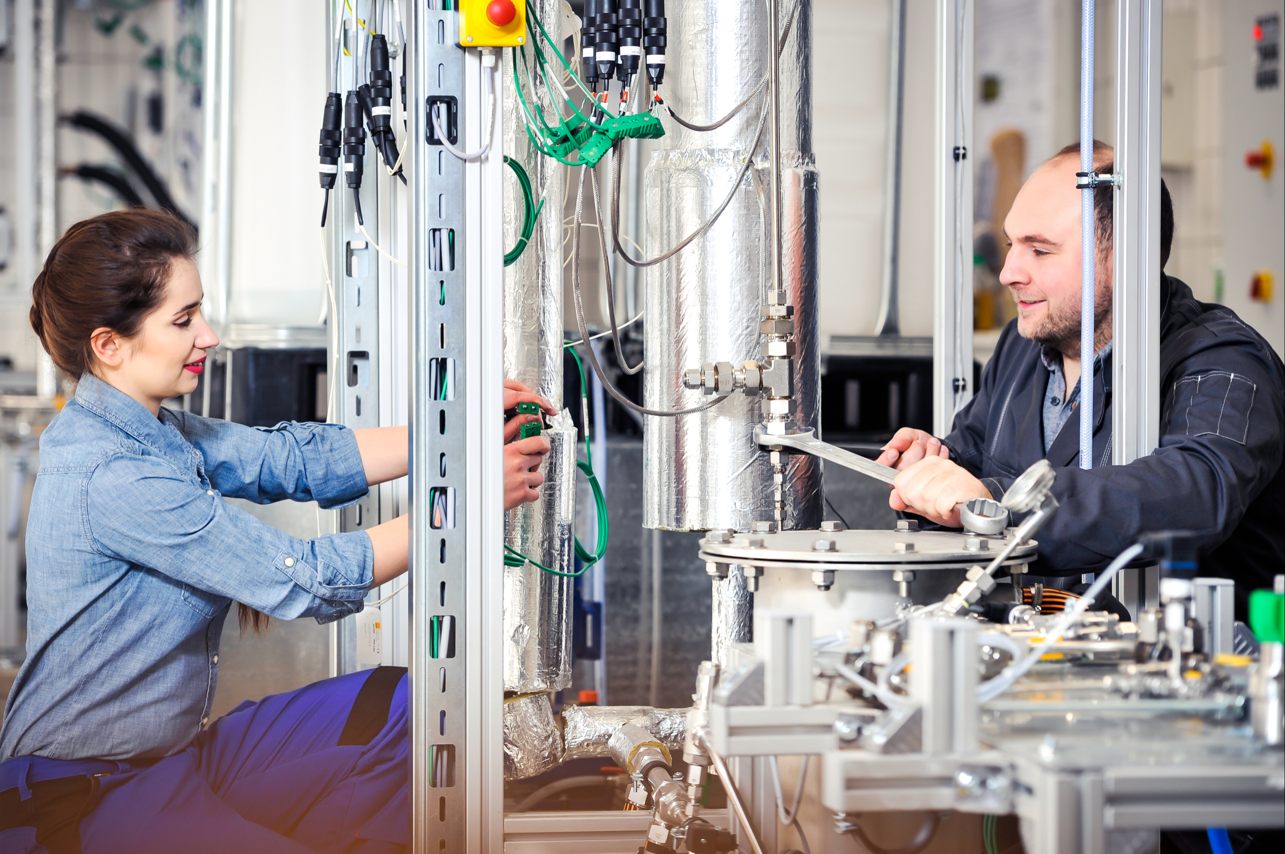 A man and a woman kneeling next to a bioreactor and  plugging individual connections.