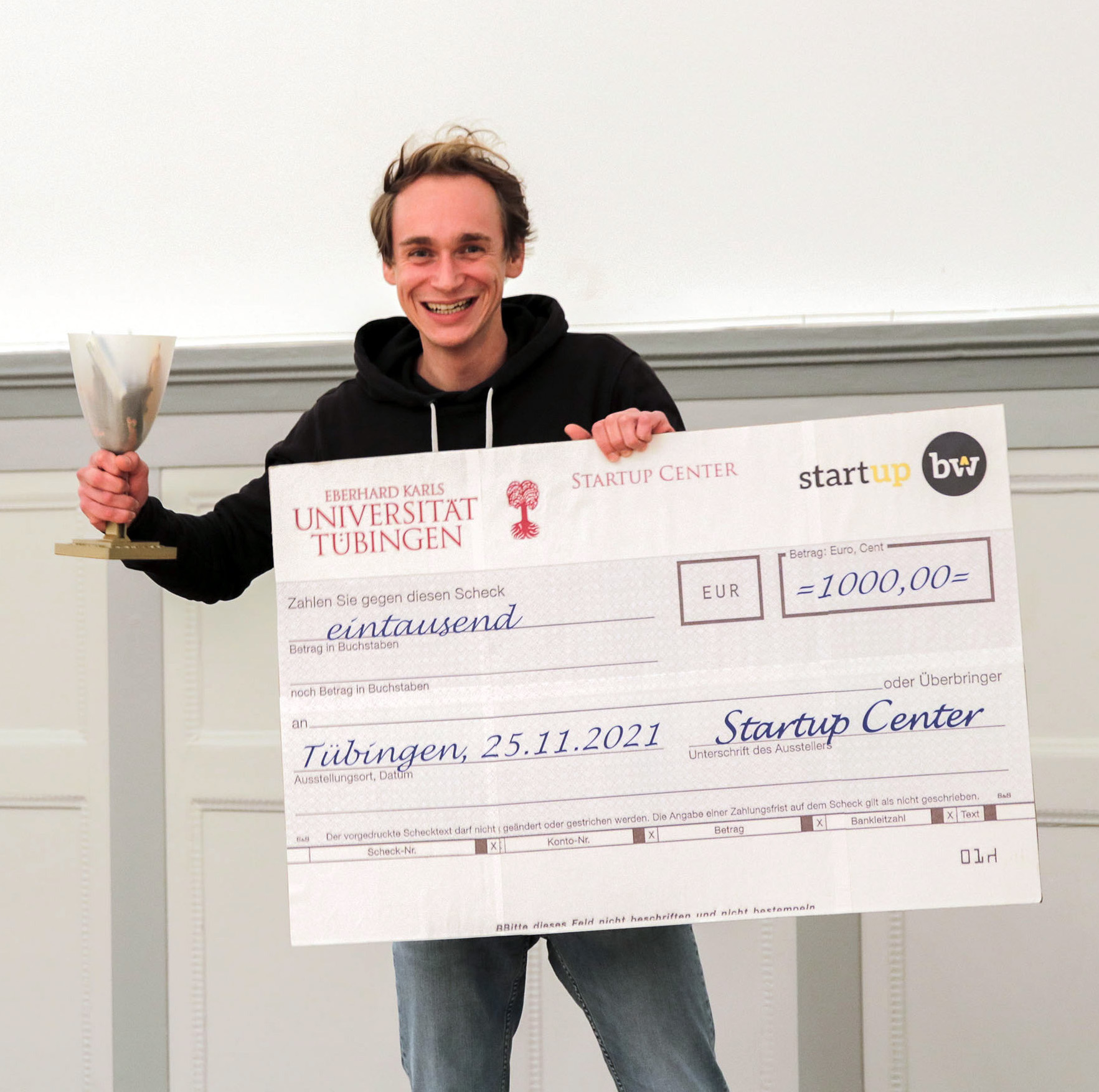 Der Umweltbiotechnologe bei der Preisverleihung mit einem Scheck und einem Pokal in der Hand.