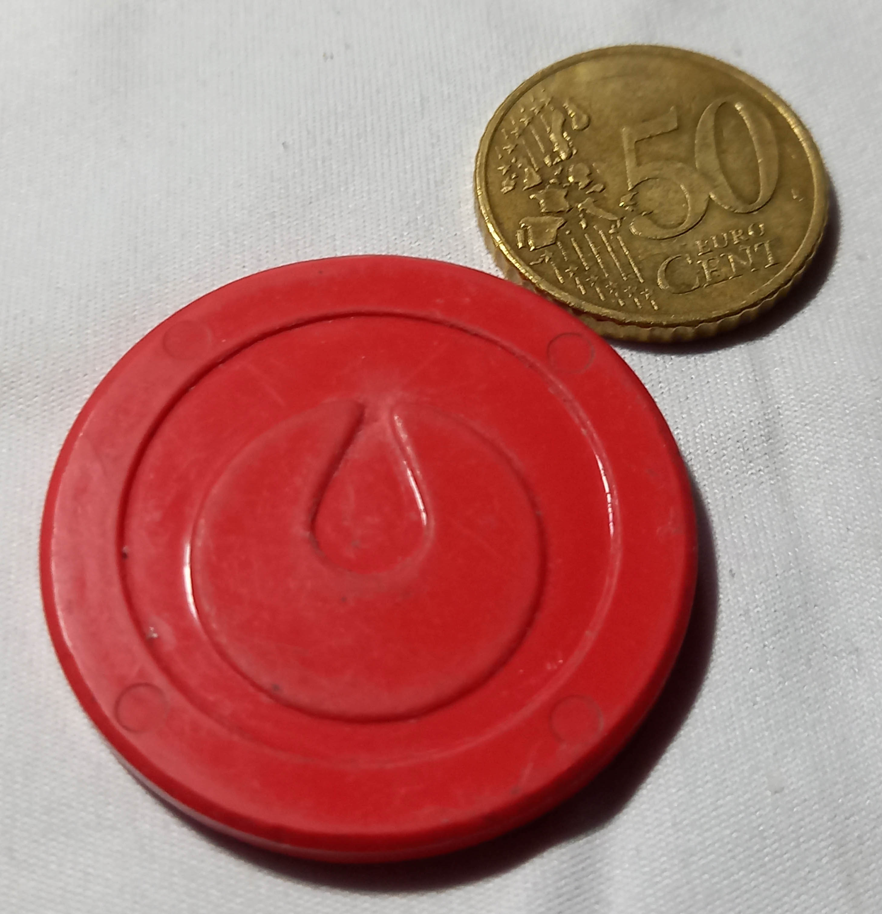 Zu sehen ist eine Biokunststoffplakette, die neben einer 50 Cent-Münze liegt und etwa doppelt so groß ist wie diese.