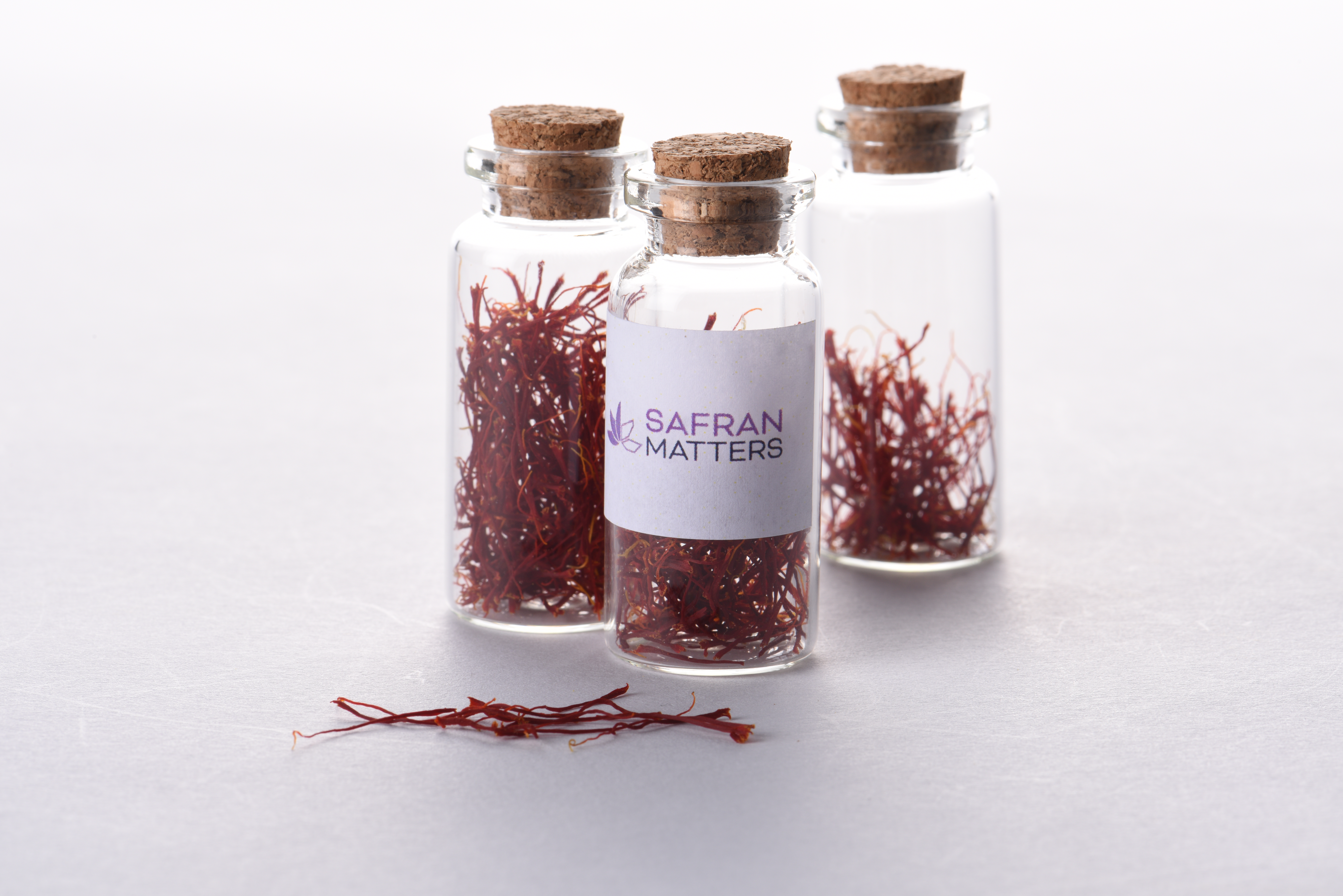 Three small glass bottles with saffron threads, in front of them are also some red saffron threads.