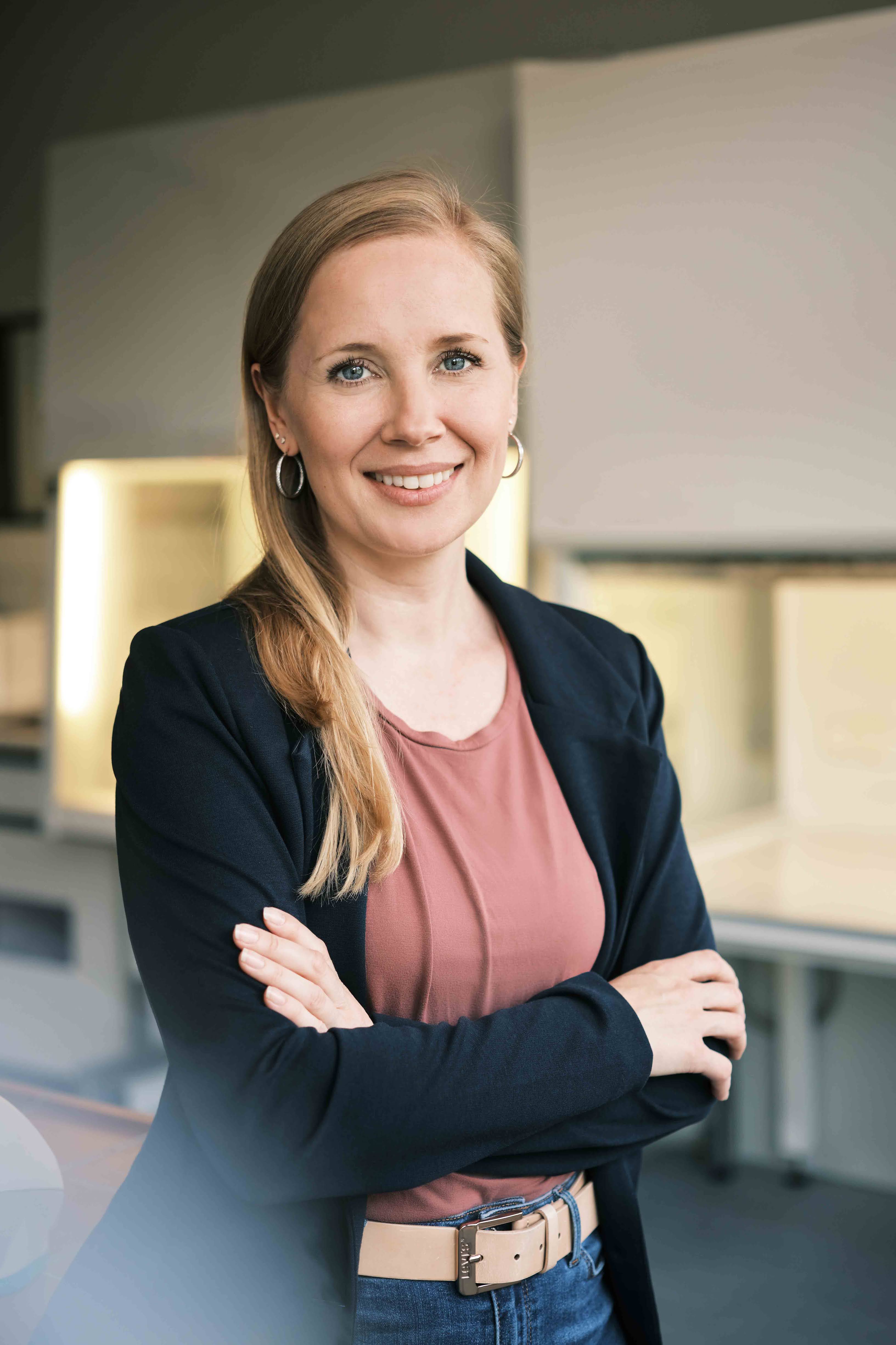 Young blonde woman in brown shirt and black jacket in front of laminar air flow lab benches