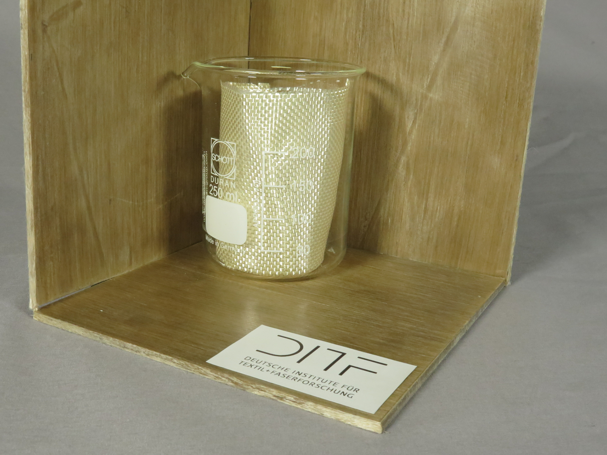 In einer Ecke aus drei Platten des Faserverbundwerkstoffs PURCELL steht ein Becherglas mit einem Stück Cellulosegewebe.