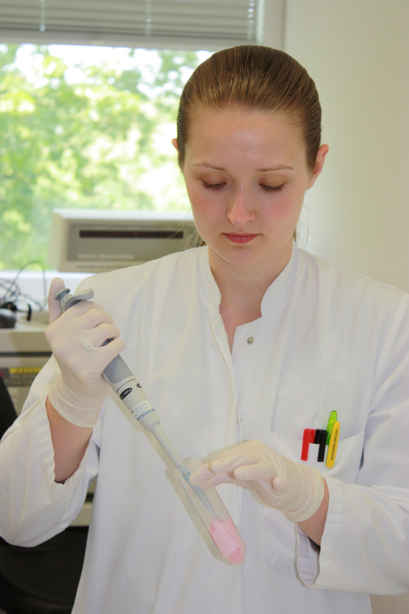 The photo shows a woman in a lab coat pipetting substances.