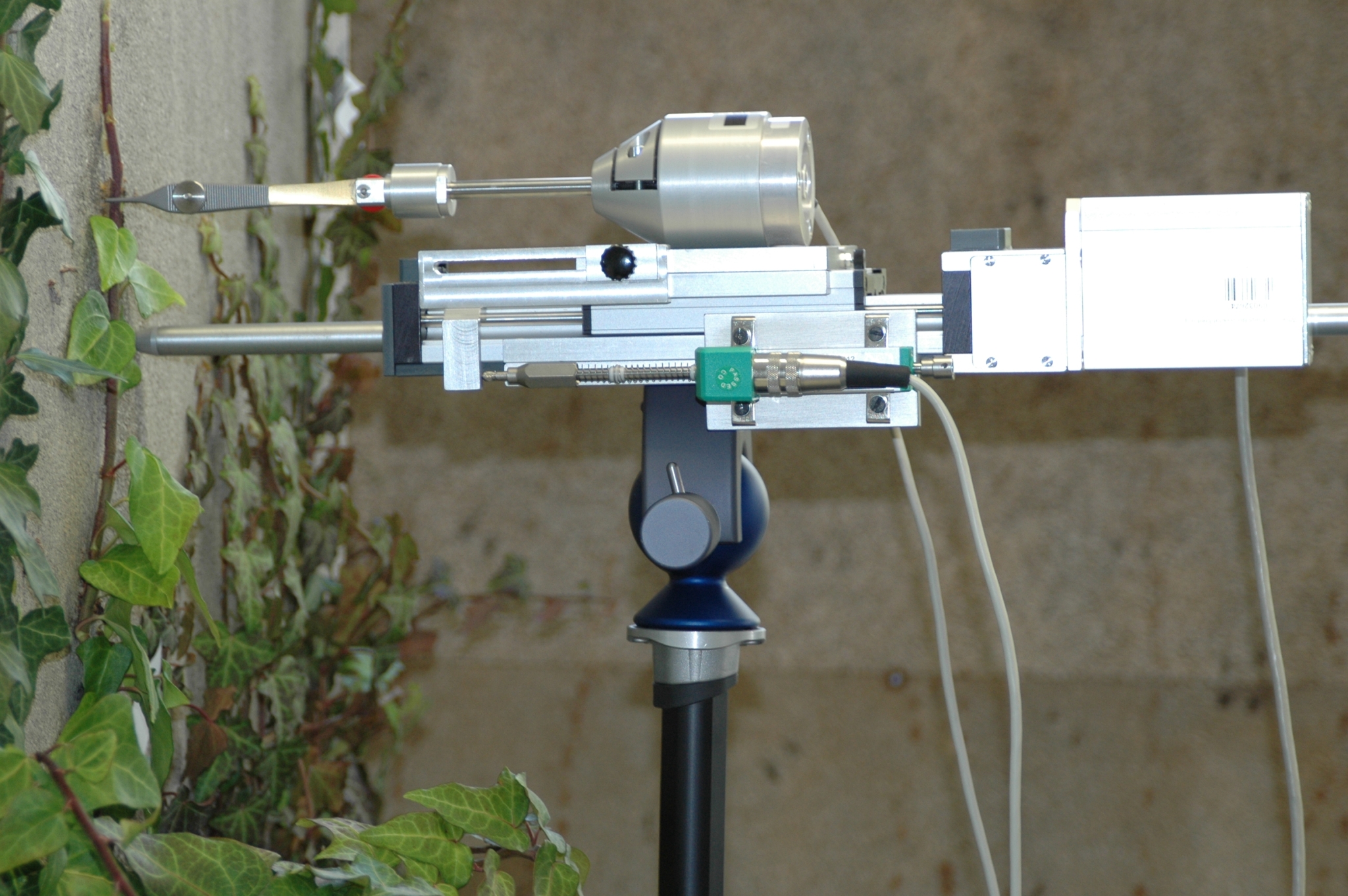 The photo shows an apparatus in front of an ivy-covered wall. The apparatus looks like a camera that is mounted onto a stand.