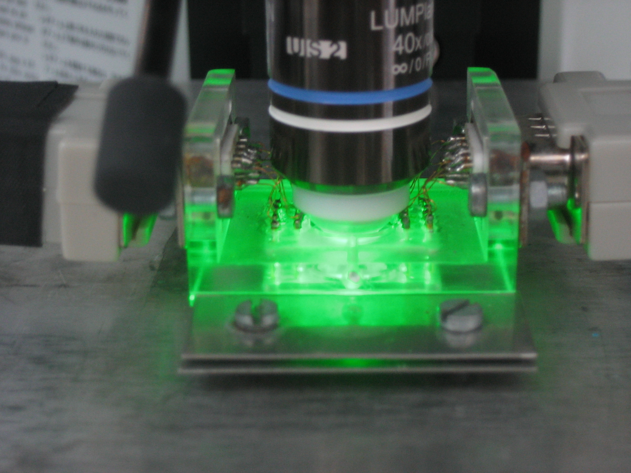 Zu sehen ist ein in eine Apparatur eingespannter Glasquader, der grünlich leuchtet.