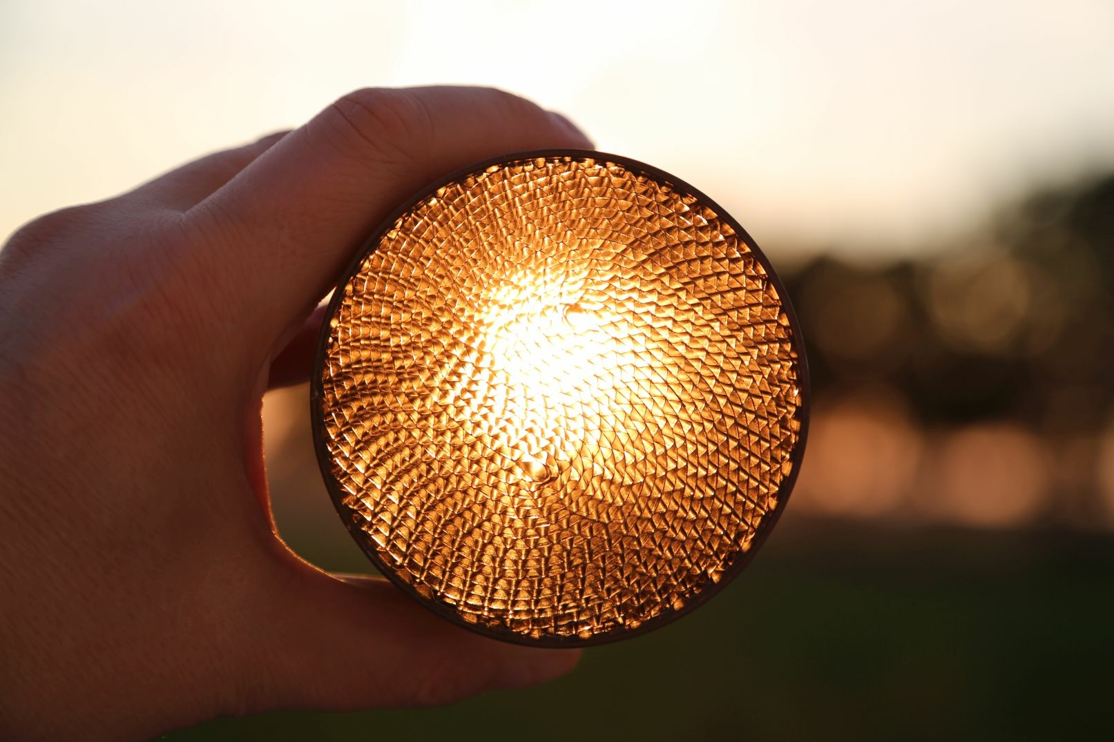 The photo shows a hand holding a honeycomb-shaped, round nickel catalyst into the sun. The honeycomb structure of the metal methanation reaction becomes thus very clear.