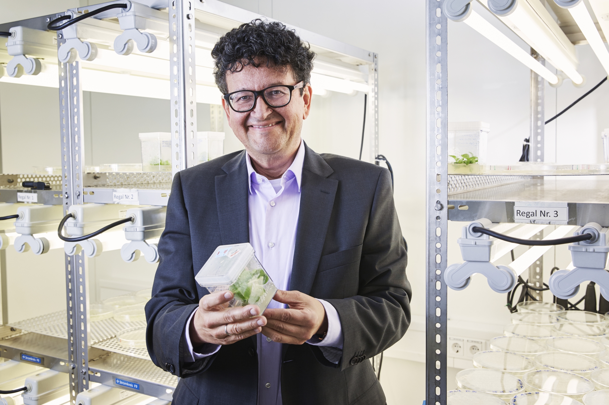 Prof. Dr. Puchta im Labor. Er hält eine kleine Tabakpflanze in In-vitro-Kultur in den Händen.