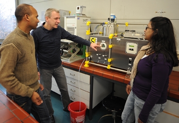 The photo shows three people standing in front of a filtering system.