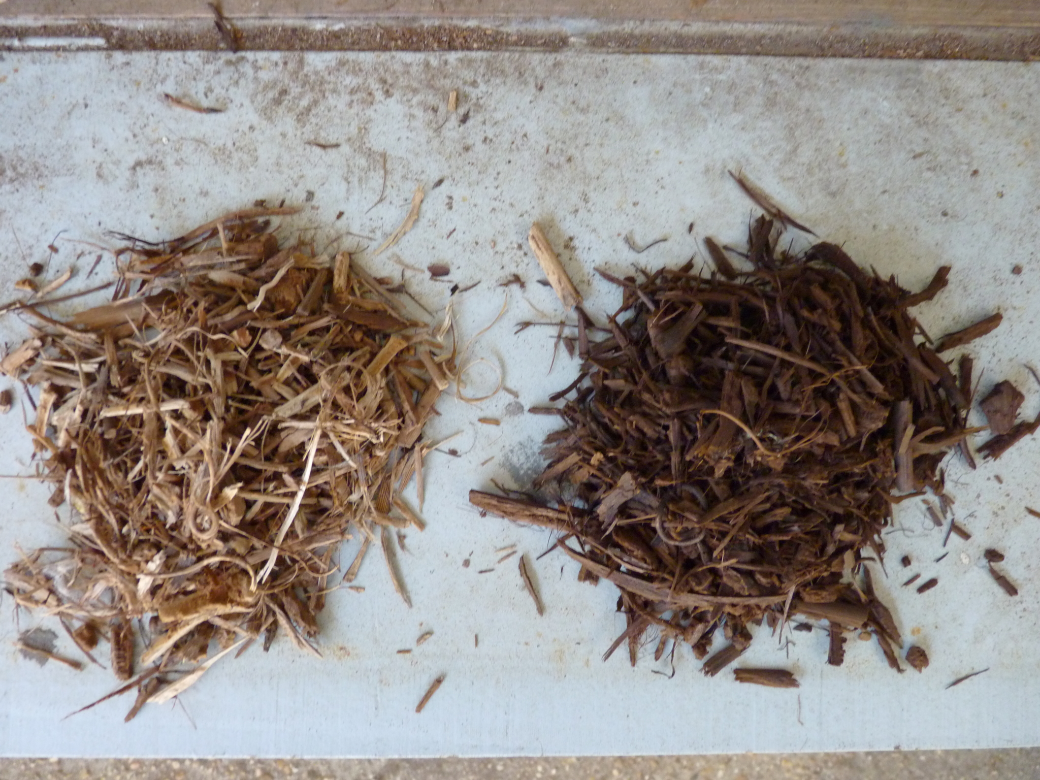 Two piles of shredded biomass (different particle sizes) shown against a neutral background. The pile on the left-hand side is characterised by a light, voluminous material. The pile on the right-hand side is composed of a more compact and darker material