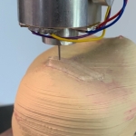 Eine hautfarbende Halbkugel, die mit einer silbernen Nadel im 3D-Drucker bedruckt wird.