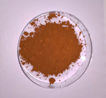 The photo shows a glass Petri dish with a pile of brown powder.