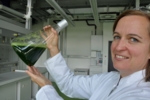 Prof. Heike Frühwirth hält einen Erlenmeyer-Kolben in die Höhe, der mit algenbedingter grüner Flüssigkeit gefüllt ist.