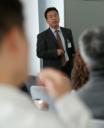Ein Asiate in einem dunklen Anzug hält eine Präsentation.