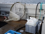Schiffsdeck auf dem Meer, das ein Fischernetz und zwei Kanister mit Flüssigkeit zeigt.