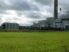 The photo shows a green field and a factory in the background.